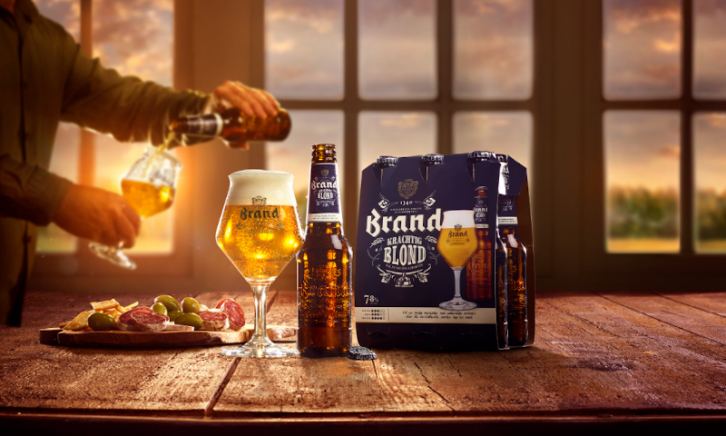 Brand Krachtig Blond sixpack en glas op tafel met hapjes ernaast